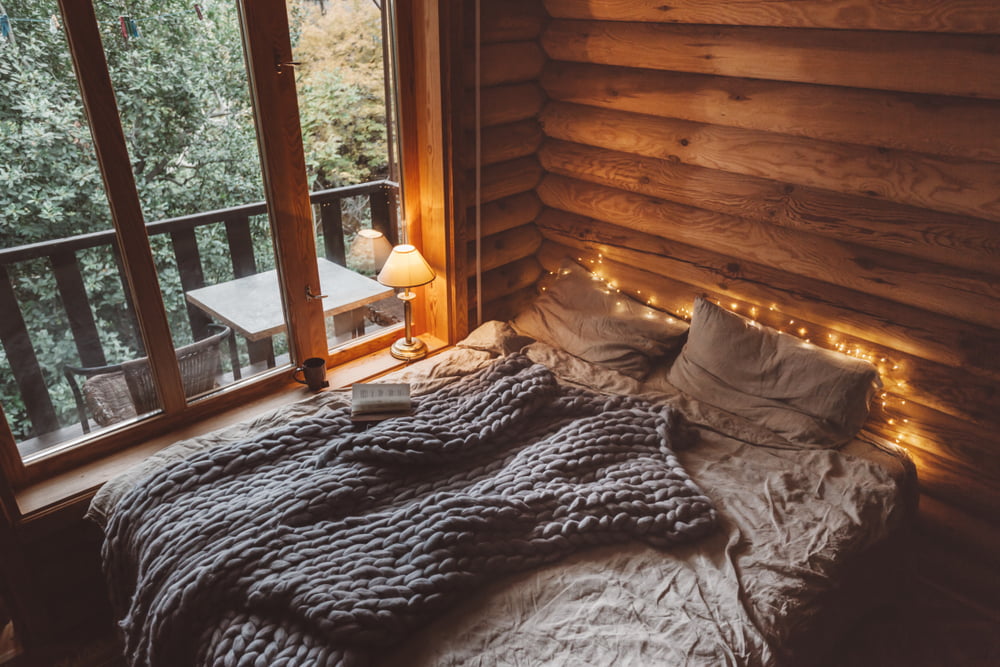 Rustic interior decoration of log cabin bedroom. Cozy warm blanket on bed by window.